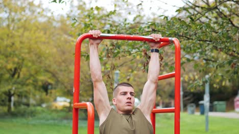 Sporty-young-man-doing-pull-ups-on-piece-of-sports-equipment-in-public-park,-tracking-shot