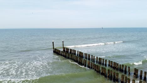 Two-seagulls-sitting-on-wooden-poles-of-a-long-groyne-reaching-into-the-sea-in-the-Netherlands