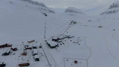 Drohnenansicht-In-Spitzbergen,-Die-über-Die-Stadt-Longyearbyen-Fliegt-Und-Häuser-In-Einem-Verschneiten-Gebiet-Mit-Bergen-Am-Horizont-In-Norwegen-Zeigt