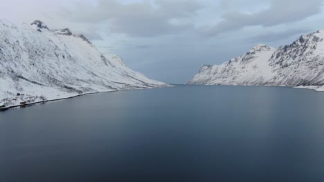 Vista-De-Drones-En-La-Zona-De-Tromso-En-Invierno-Volando-Sobre-Un-Fiordo-Azul-Rodeado-De-Montañas-Blancas-Nevadas-En-Noruega