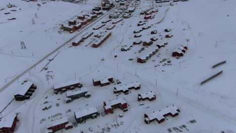Drone-view-in-Svalbard-flying-over-Longyearbyen-town-showing-houses-in-a-snowy-area-with-a-fjord-and-mountain-in-Norway