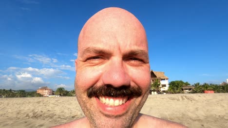Close-up-of-caucasian-male-with-moustache-smiling-in-front-of-camera-at-beach
