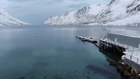 Drone-view-in-Tromso-area-in-winter-vertical-lift-showing-a-pebbled-beach-and-a-fjord-surrounded-by-white-snowy-mountains-in-Norway