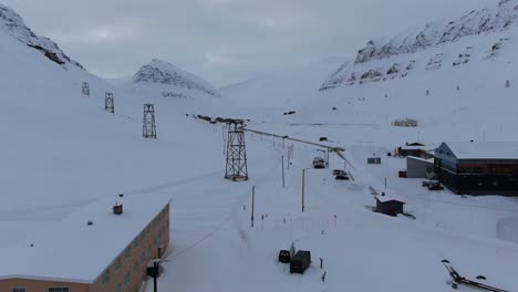 Vista-De-Drones-En-Svalbard-Volando-Sobre-La-Ciudad-De-Longyearbyen-Mostrando-Casas-En-Una-Zona-Nevada-Con-Montañas-En-El-Horizonte-En-Noruega