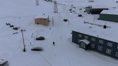 Drone-view-in-Svalbard-flying-over-Longyearbyen-town-showing-a-person-in-a-black-coat-walking-between-houses-in-a-snowy-area-with-mountains-in-Norway