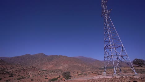 High-Voltage-Electric-Tower-in-Mountainous-Landscape-Against-a-Clear-Blue-Sky,-Revealing-pan,-panoramic-view