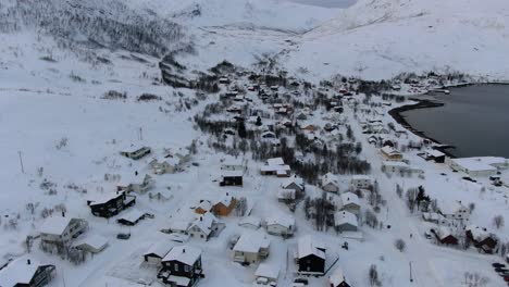 Drone-view-in-Tromso-area-in-winter-flying-over-a-small-town-with-a-full-of-snow-landscape-and-white-mountains-next-to-a-fjord-in-Norway