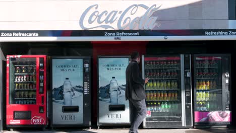 Ein-Käufer-Kauft-Wasser-An-Einem-Getränkeautomaten,-Während-Zahlreiche-Snacks-Und-Limonaden-Wie-Coca-Cola-Und-Fanta-Zum-Kauf-Bereitstehen