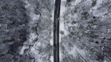Car-driving-on-a-road-leading-through-a-forest-covered-in-snow-during-winter