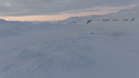 Drone-view-in-Svalbard-flying-over-snowy-white-mountains-with-frozen-lakes-in-Norway-on-a-cloudy-day
