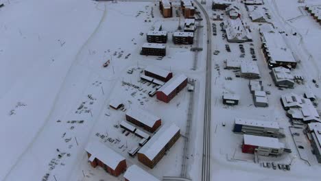Drone-view-in-Svalbard-flying-over-Longyearbyen-town-showing-houses-in-a-snowy-area-with-card-on-a-road-top-view-in-Norway
