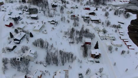 Vista-De-Drones-En-La-Zona-De-Tromso-En-Invierno-Volando-Sobre-Un-Pequeño-Pueblo-Con-Un-Paisaje-Lleno-De-Nieve-Y-Un-Coche-En-Movimiento-Junto-A-Un-Fiordo-En-Noruega