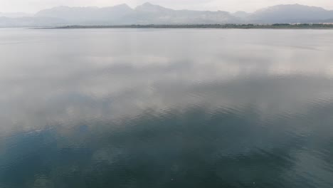 Vista-De-Drones-En-Albania-Volando-Sobre-El-Lago-De-Color-Verde-Shkodër-En-La-Vista-Superior-De-Pogradec-En-Un-Día-Nublado-Y-Montañas-En-El-Horizonte
