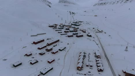 Drone-view-in-Svalbard-flying-over-Longyearbyen-town-showing-houses-in-a-snowy-area-with-mountains-in-the-horizon-in-Norway