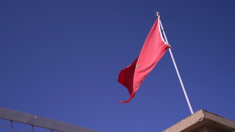 Moroccan-Flag-waving-in-a-Restricted-Area,-Set-Against-a-Clear-Blue-Sky