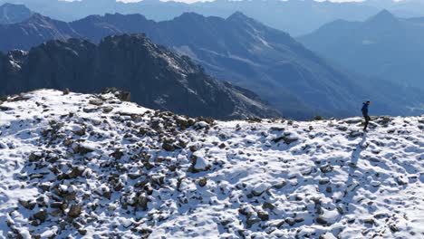 Hiker-explorer-walking-on-snowy-ridge-mountain-with-breathtaking-views-of-Alps-range-in-background,-Cima-Fontana,-Valmalenco-in-Italy