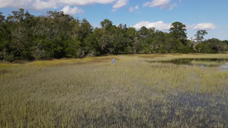 fisherman-walking-slowly-and-carefully-thru-the-grass-of-wetlands-in-south-carolina-marsh-during-a-sunny-day