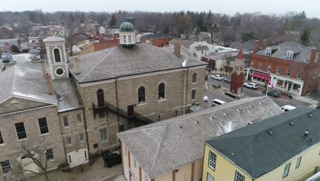 A-drone-captures-an-aerial-view-of-Niagara-on-the-Lake's-downtown-courthouse,-on-a-quaint-old-street-filled-with-shops,-as-light-snow-falls-in-winter