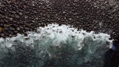 Ocean-waves-gently-crashing-into-pebbles-beach,-view-from-above,-tilt-down