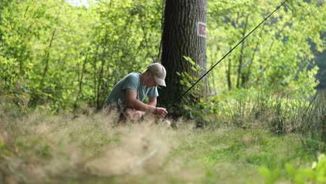 Male-angler-prepares-his-fishing-rod-and-equipment-in-the-grass