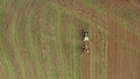 Top-down-aerial-follow-shot-over-a-green-tractor-ploughing-a-field