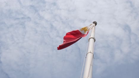 Die-Nach-Links-Wehende-Philippinische-Nationalflagge-Wurde-Von-Unten-Gefilmt,-Während-Die-Kamera-Herauszoomt-Und-Baumwollartige-Wolken-Freigibt