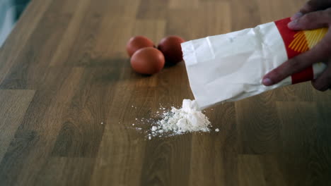 Pouring-Flour-on-Wooden-Surface-for-Baking-with-Eggs-in-Background