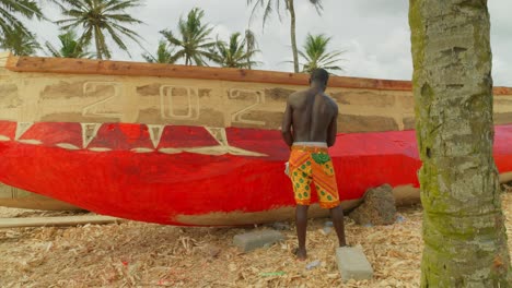 black-male-painting-a-wooden-fisherman-boat-in-red-during-maintenance-work