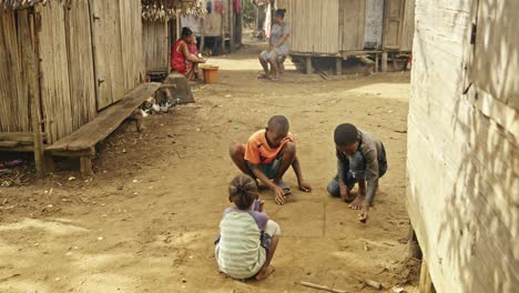 Malagasy-children-squat-between-wooden-houses-and-play-in-the-dust-with-marbles---static-shot