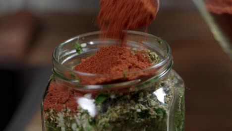 Adding-red-pepper-with-a-spoon-to-the-chimichurri-sauce-in-the-glass-container-where-it-is-kept