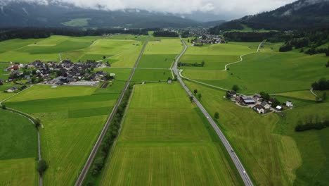 Alpine-Serenity:-4K-Aerial-Drone-Shot-of-Foggy-Drive-from-Graz-to-Hallstatt,-Cars-Wind-Through-Austrian-Countryside-with-perfectly-mowed-green-fields-and-Breathtaking-Alps-Panorama