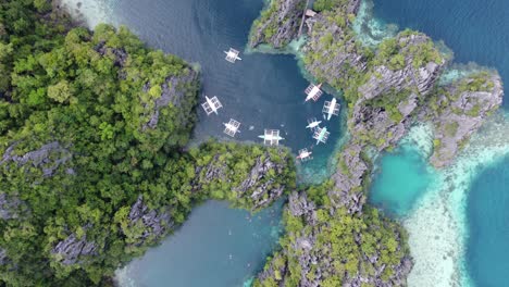 Boats-and-people-in-clear-water-amid-lush-karst-cliffs-at-twin-lagoon,-coron