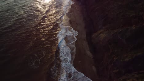 Aerial-4K-Drone-footage-of-over-the-waves-off-the-coast-of-the-Isle-of-Wight-and-then-panning-up-to-the-sun-setting-over-the-sea