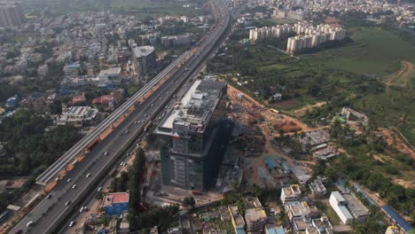 Aerial-footage-of-an-Indian-highway-that-is-expanding-quickly,-with-a-service-road,-fast-moving-automobiles,-and-commercial-and-residential-buildings