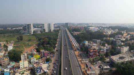 Aerial-view-of-a-rapidly-developing-Indian-highway-featuring-a-service-road,-fast-moving-cars,-and-the-construction-of-a-metro-train-bridge