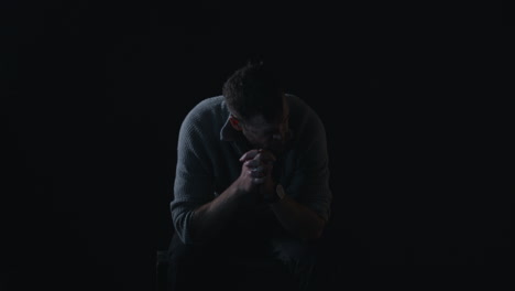 Depressed-man-sits-in-darkness-shaking-head