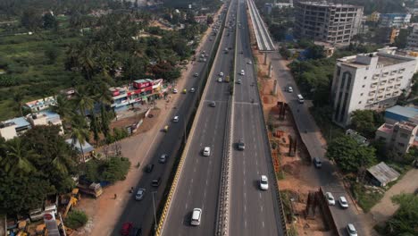 Cinematic-aerial-footage-reveals-a-service-road,-swiftly-driving-cars,-and-residential-commercial-buildings-on-an-Indian-highway-that-is-rapidly-growing