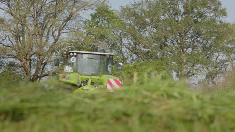Low-angle-view-from-grass-of-a-tractor-moving-across-a-meadow