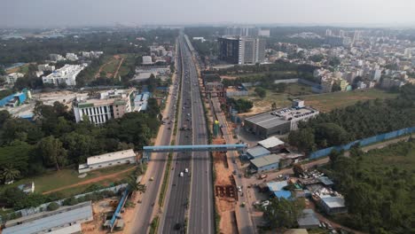 Indian-Motorway-in-a-cinematic-aerial-shot-with-metro-train-bridge-construction-visible-above-the-service-road-and-fast-moving-automobiles