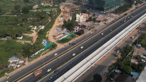 An-aerial-view-of-an-Indian-highway-that-is-expanding-quickly,-with-a-service-road,-fast-moving-automobiles,-and-a-metro-train-bridge-under-construction