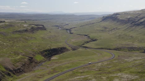 Aerial-video-as-vehicles-pass-along-a-winding-road-cutting-through-lush-green-valley-in-Western-Iceland