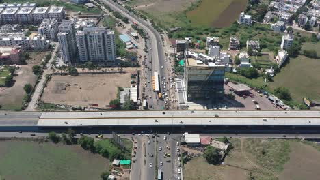 RAJKOT-CITY-AERIAL-VIEW-Drone-camera-coming-down-where-there-is-a-lot-of-traffic-next-to-the-complex-and-lots-of-bikes-and-four-wheel-trucks-are-parked-in-the-parking-lot