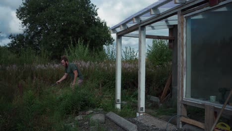 A-Man-is-Trimming-the-Wild-Plants-Around-the-Greenhouse-in-Indre-Fosen,-Norway---Timelapse