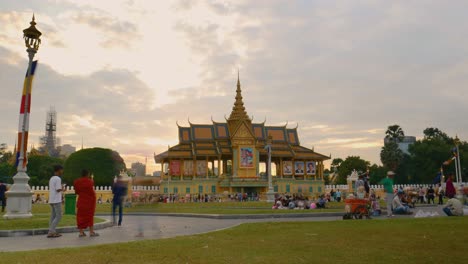 Los-Turistas-Se-Reúnen-En-El-Césped-Para-Visitar-El-Palacio-Real-En-Phnom-Penh,-Camboya,-Al-Atardecer.