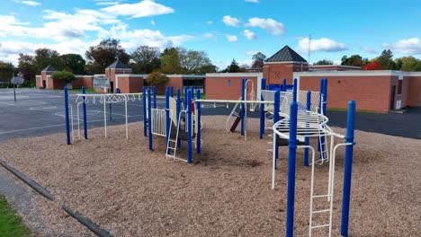 Playground-with-blue-and-white-equipment-on-wood-chips,-next-to-a-school-and-basketball-court