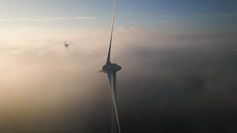Fog-and-clouds-move-between-rotating-blades-of-large-wind-turbines-during-sunrise