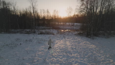 Man-in-white-jacket-walks-towards-sunset-in-snowy-field