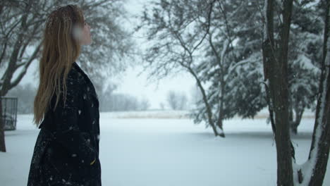 Woman-walking-outside-in-slow-motion,-watching-Christmas-winter-snow-as-snowflakes-fall-in-cinematic-slow-motion