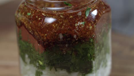 Glass-jar-with-ingredients-for-chimichurri,-fresh-parsley,-oregano,-ground-red-pepper,-black-pepper,-salt,-garlic-and-more