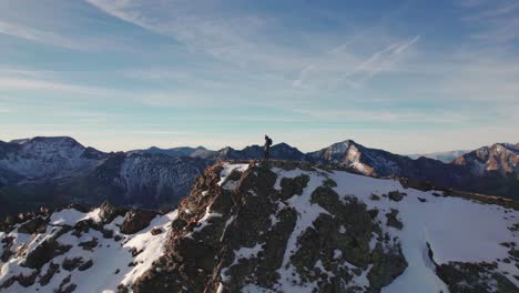 Aerial-orbit-view-of-a-man-standing-on-top-of-a-snowy-mountain-peak-in-French-Pyrenees